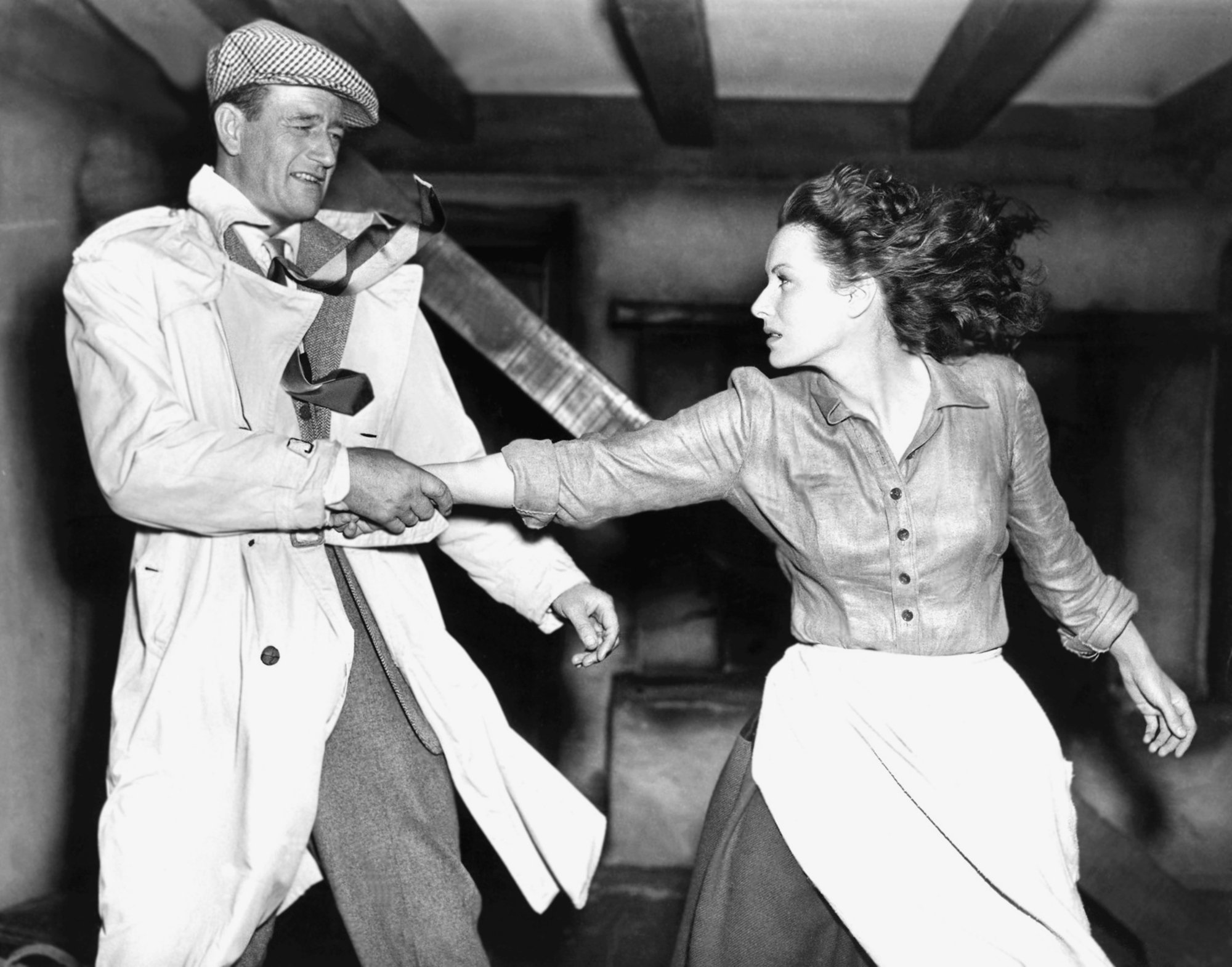 'The Quiet Man' John Wayne and Maureen O'Hara. Wayne's wearing a trench coat and yanking O'Hara by the arm toward him, who is wearing an apron.