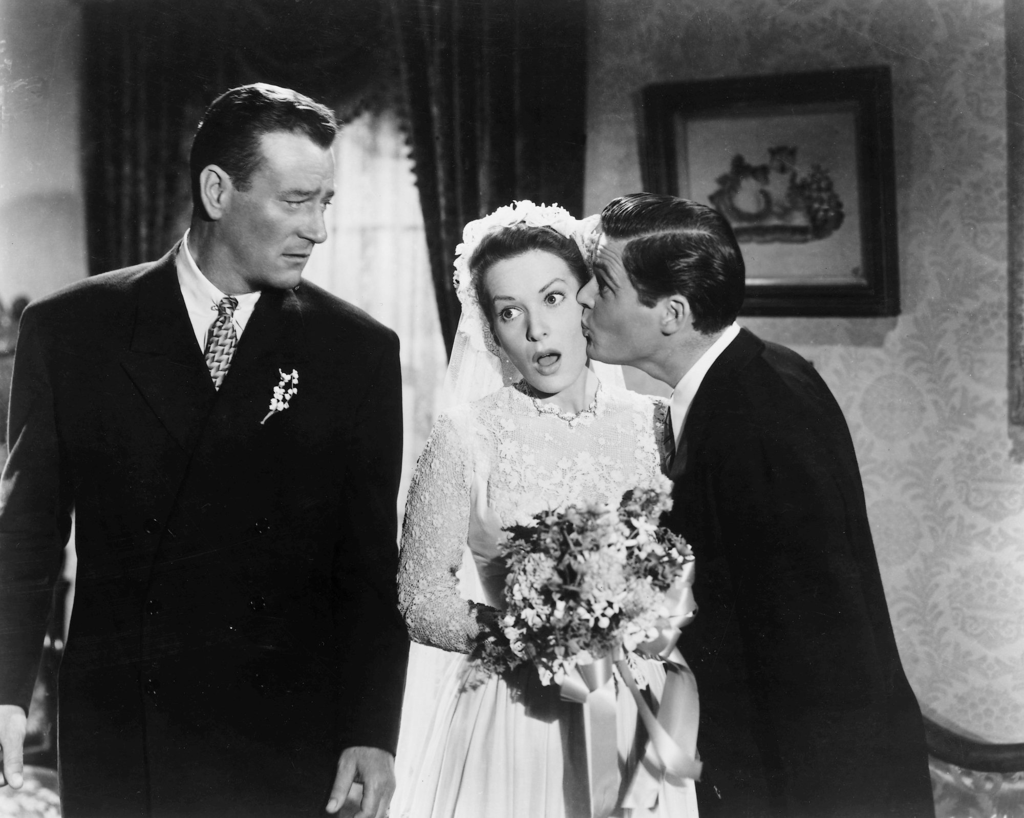 'The Quiet Man' John Wayne as Sean Thornton and Maureen O'Hara as Mary Kate Danaher. Wayne is wearing a suit and O'Hara is wearing a wedding dress as she's getting a kiss on the cheek.