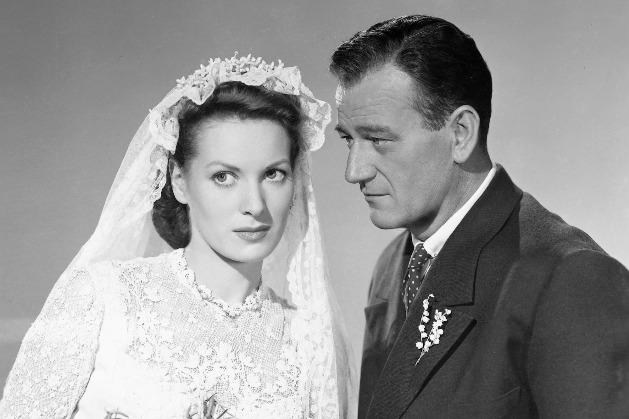 'The Quiet Man' Maureen O'Hara as Mary Kate Danaher and John Wayne as Sean Thornton. O'Hara is wearing a wedding dress looking to her right. Wayne is wearing a suit facing directly toward O'Hara.