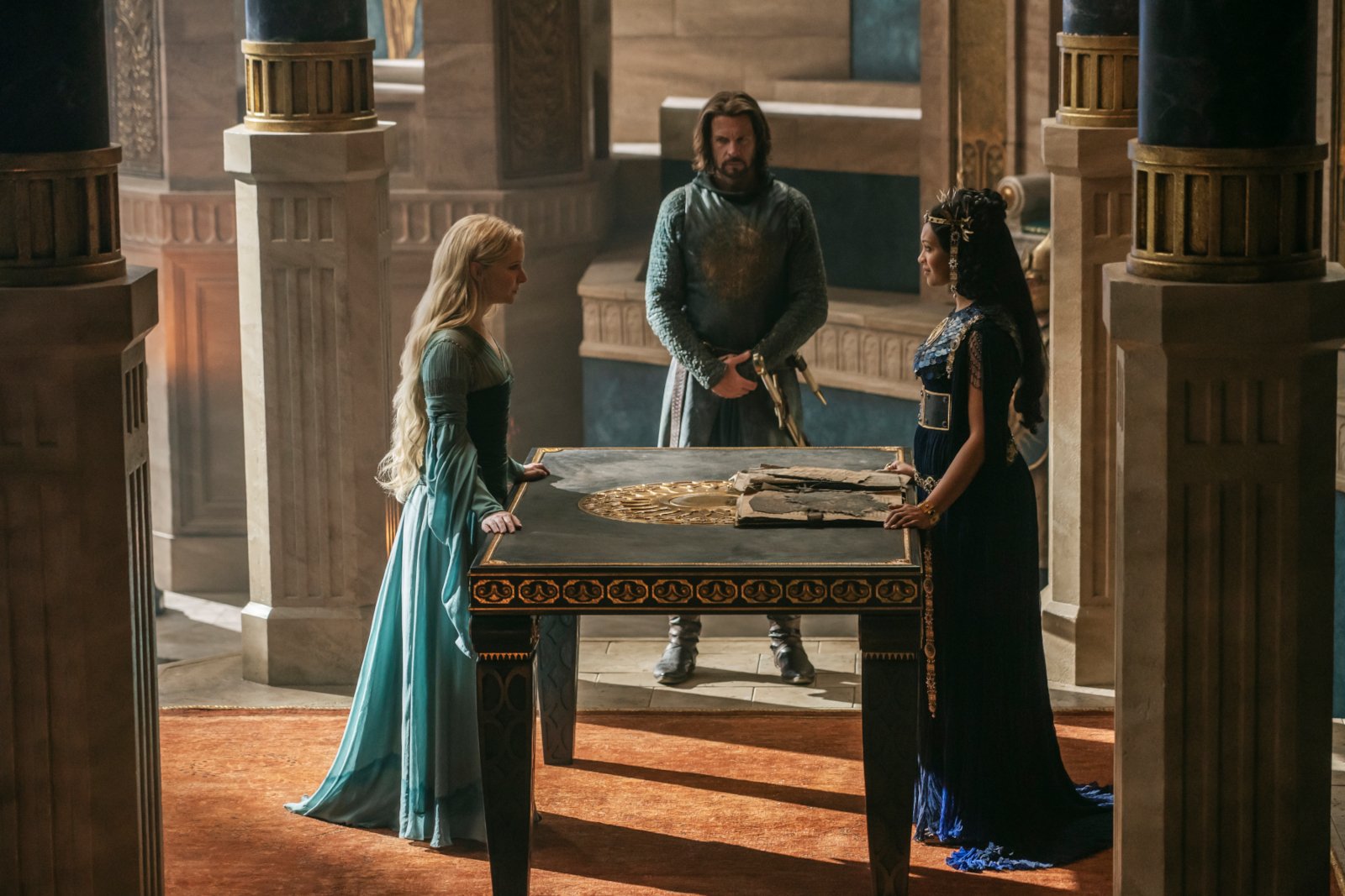 「The Rings of Power」エピソード 4 の Morfydd Clark (Galadriel)、Lloyd Owen (Elendil)、および Cynthia Addai-Robinson (Queen Regent Míriel)。彼らはテーブルの周りに立っています。