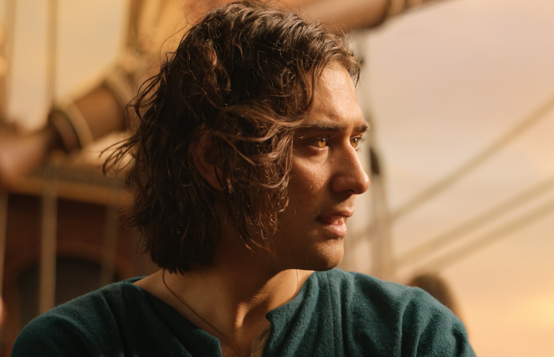 Maxim Baldry as Isildur for our article about the foreshadowing in 'The Rings of Power' Episode 5. In the photo, he's wearing a green shirt, on a ship, and looking out at the sea.