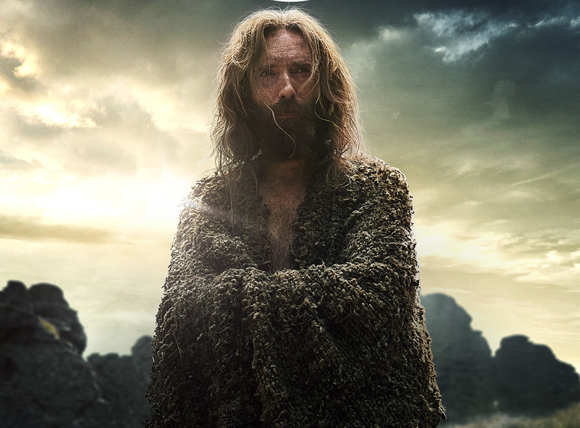Daniel Weyman as The Stranger in 'The Lord of the Rings: The Rings of Power.' He's standing with his arms crossed.