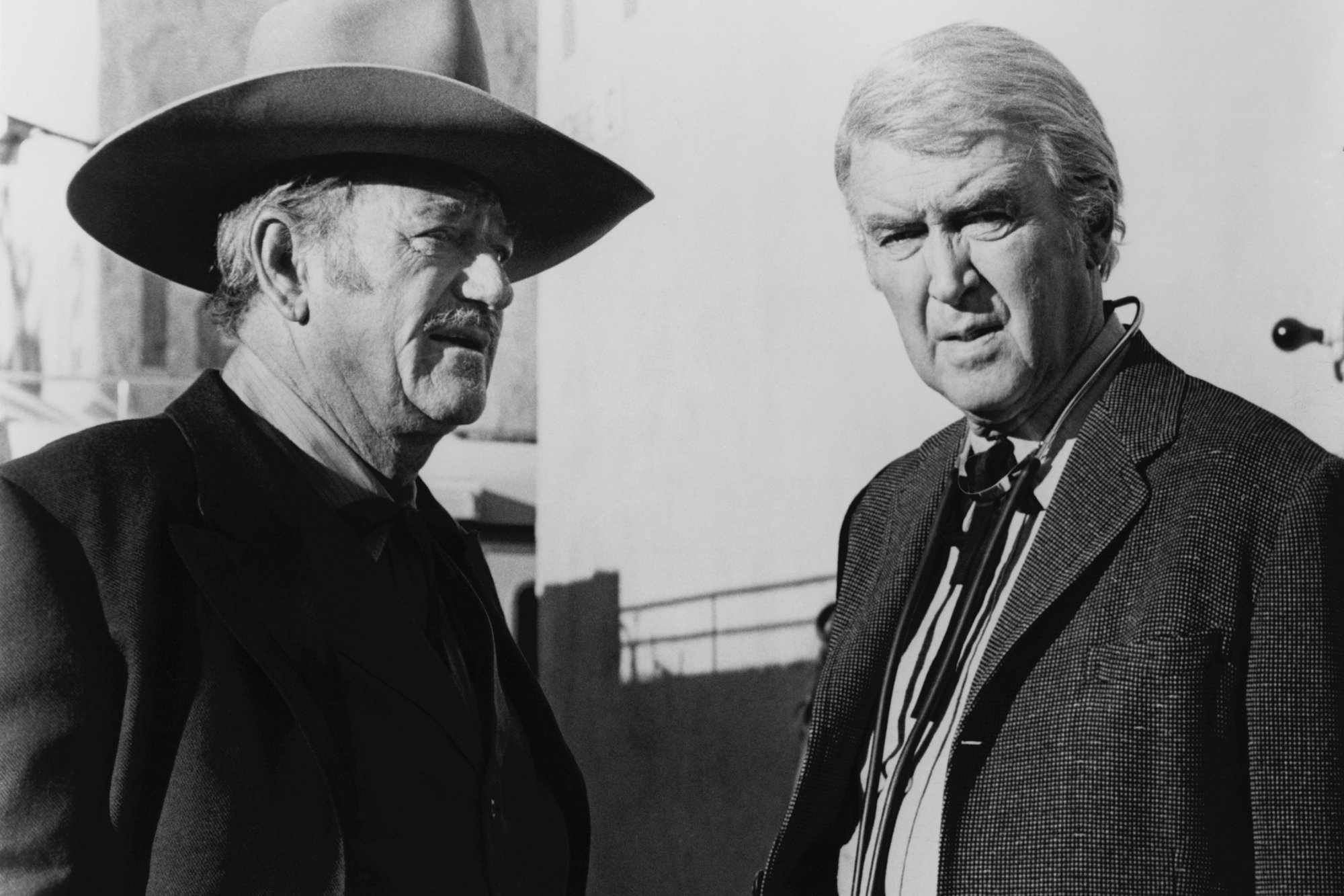 'The Shootist' John Wayne and Jimmy Stewart in black-and-white picture wearing their Western costumes. Stewart is looking at the camera and Wayne is looking off-camera.