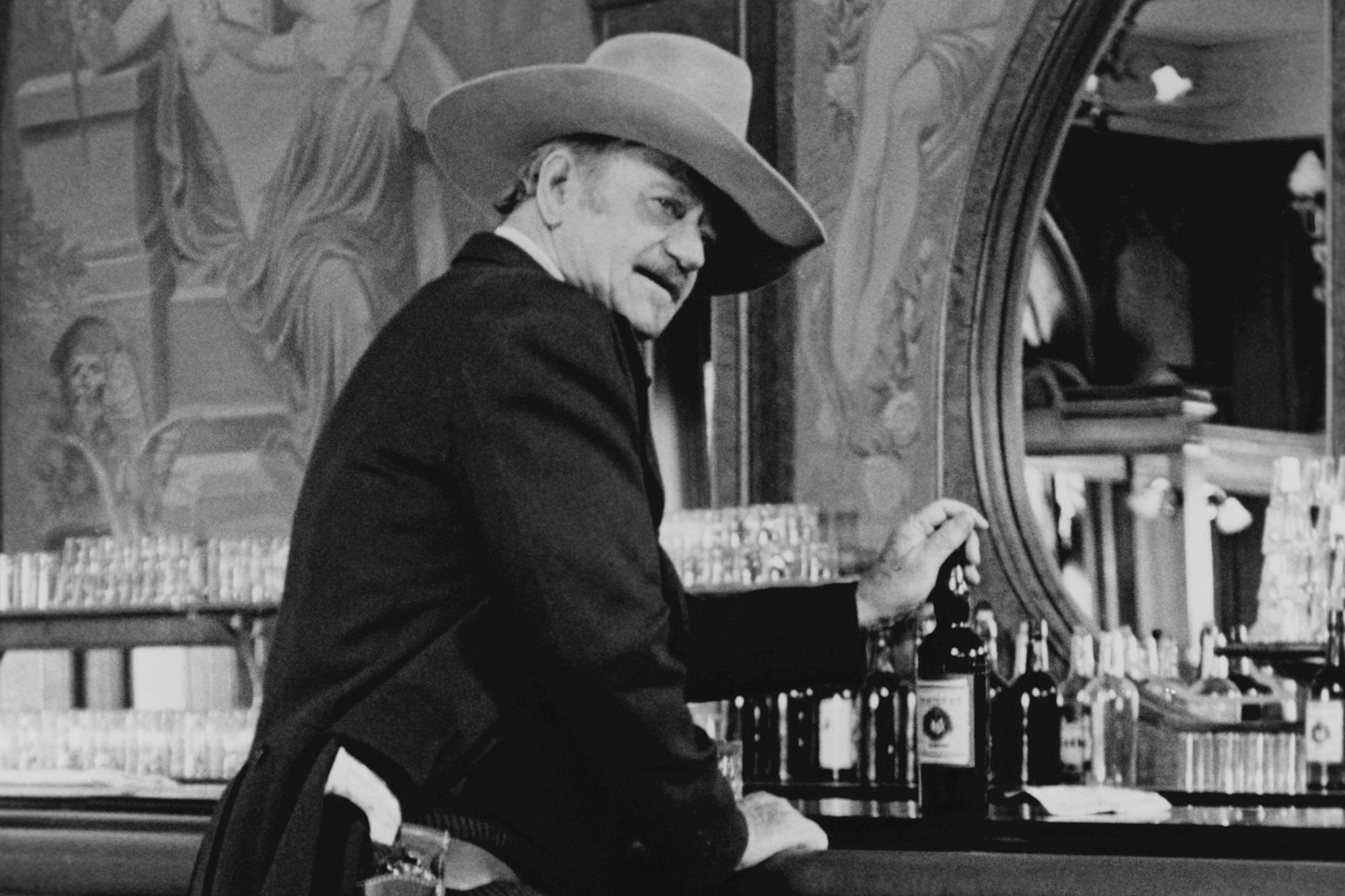 'The Shootist' actor John Wayne as J.B. Books standing at a bar while he's wearing a Western movie costume