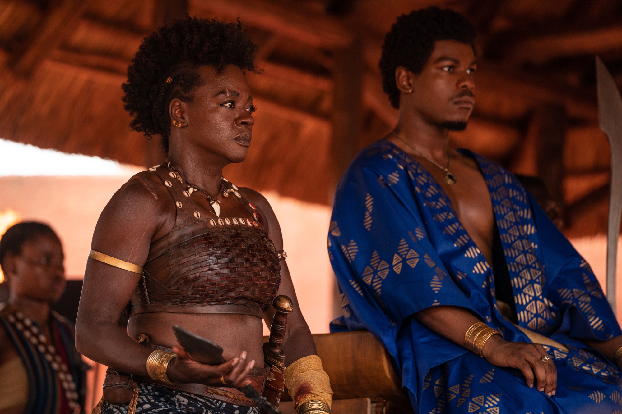 'The Woman King' Viola Davis as Nanisca and John Boyega as King Ghezo. They sit under a shade covering, looking ahead.