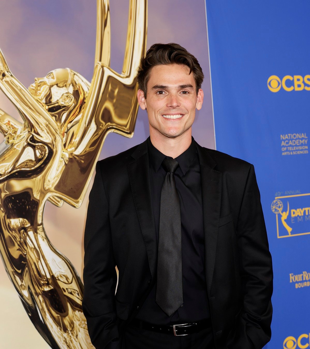 'The Young and the Restless' star Mark Grossman in a black suit and posing in front of an Emmy picture.