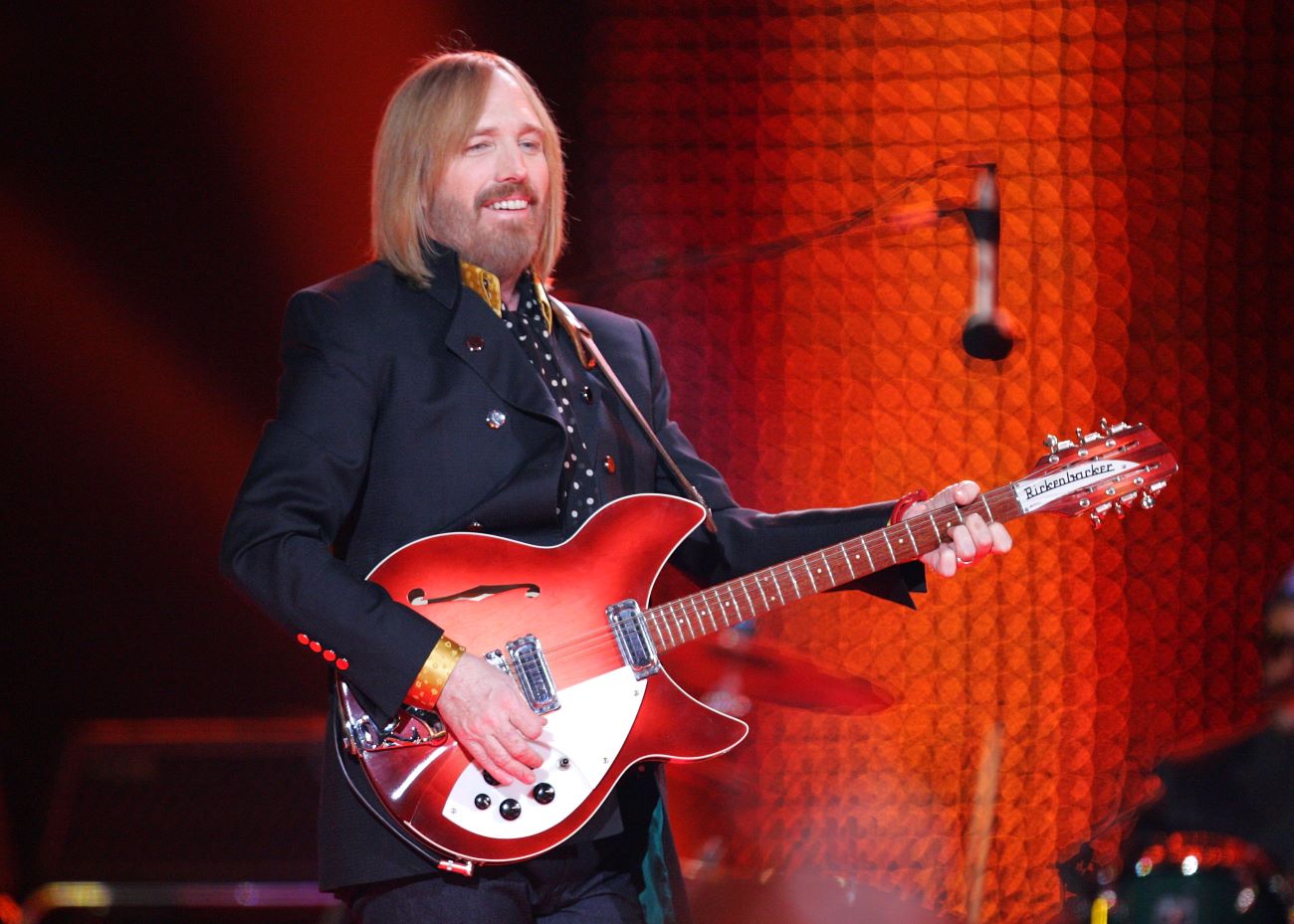 Tom Petty stands on stage and plays the guitar. 