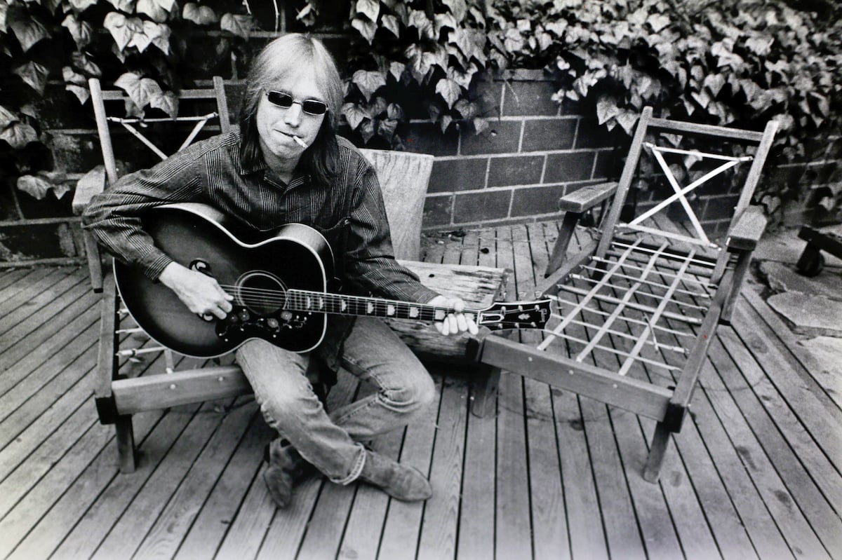 Musician Tom Petty sits on a chair while smoking a cigarette at his home in 1985