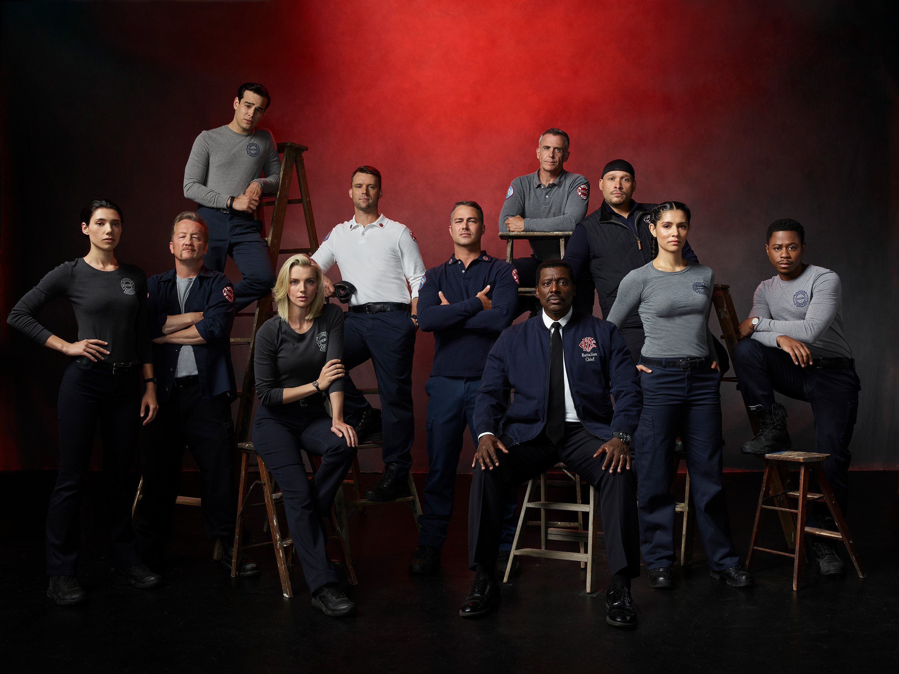 The Chicago Fire cast poses in front of a red background.