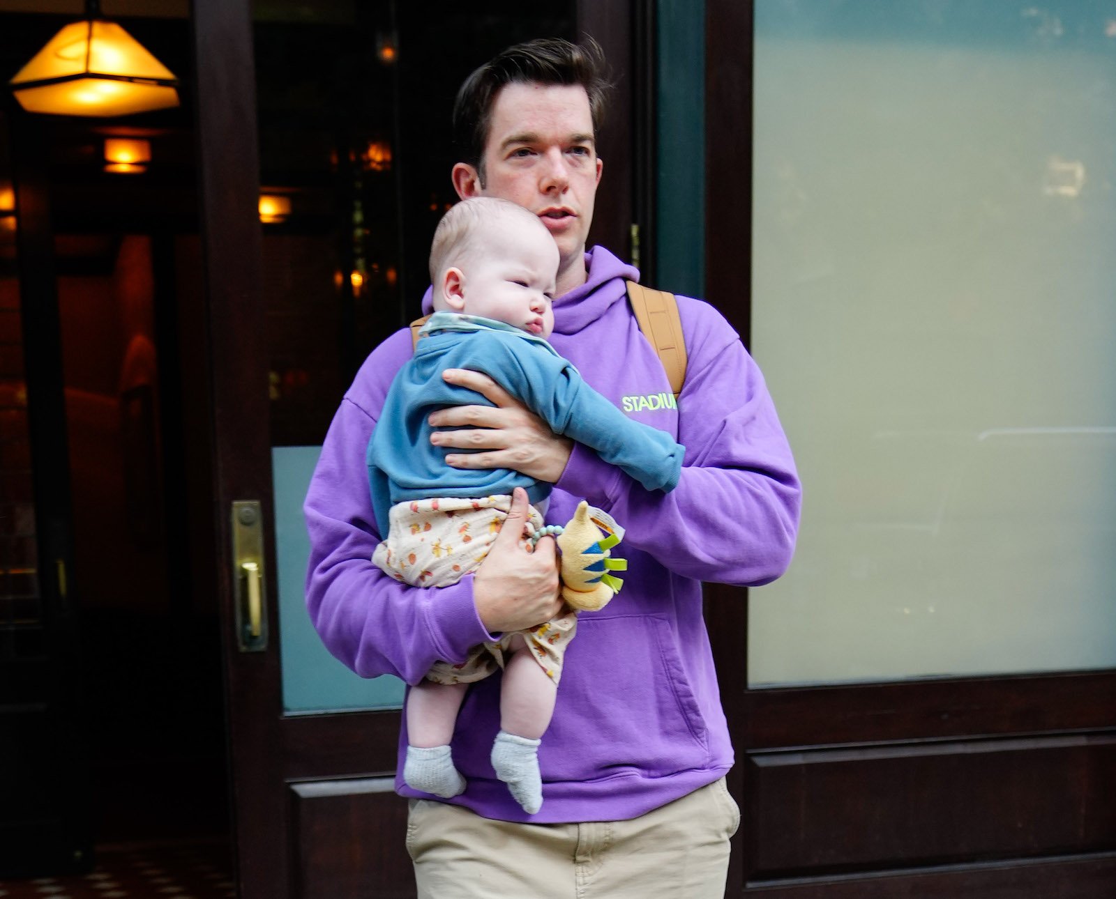 John Mulaney leaves a hotel while holding his infant son