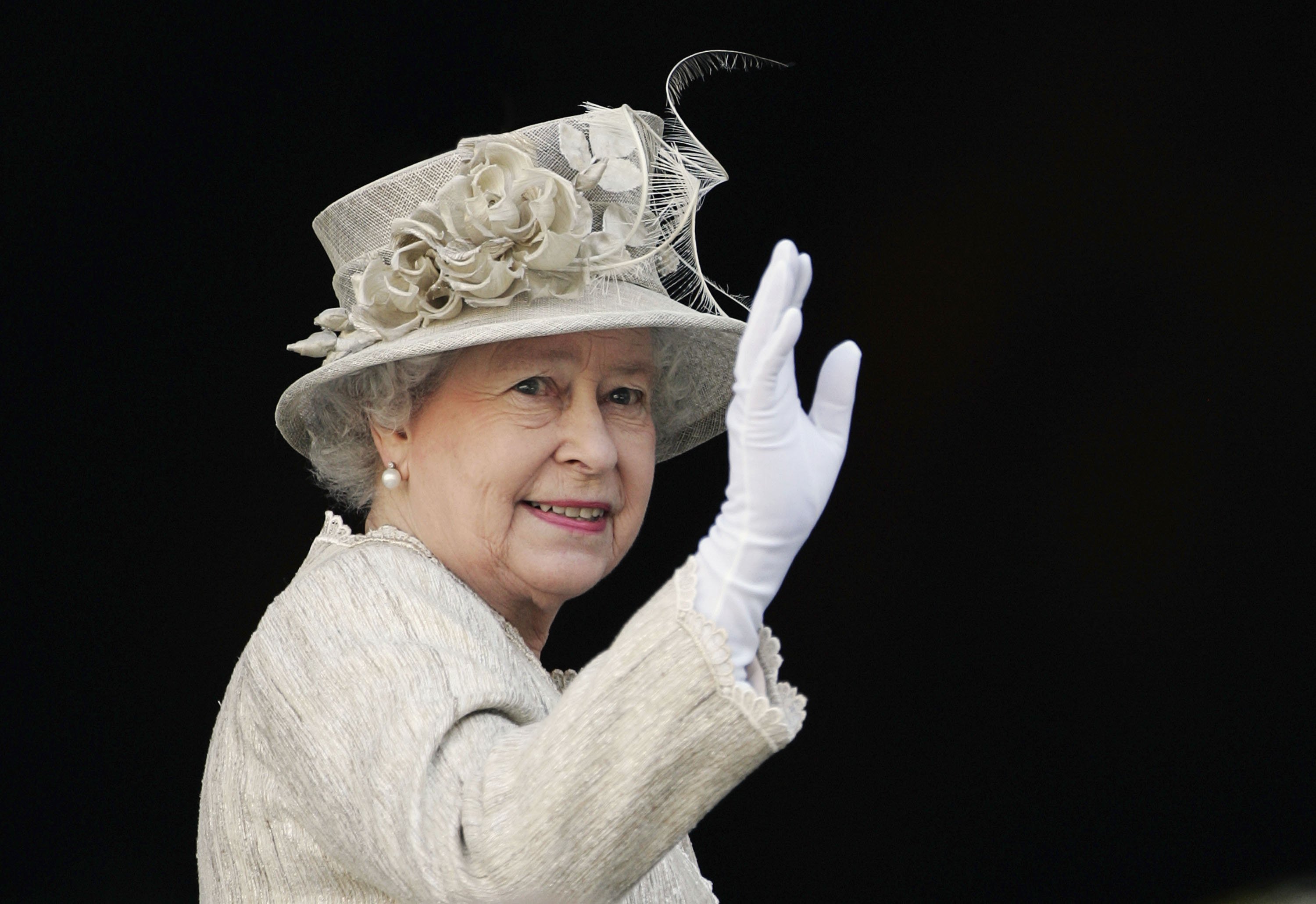 Queen Elizabeth waves while wearing a white outfit.