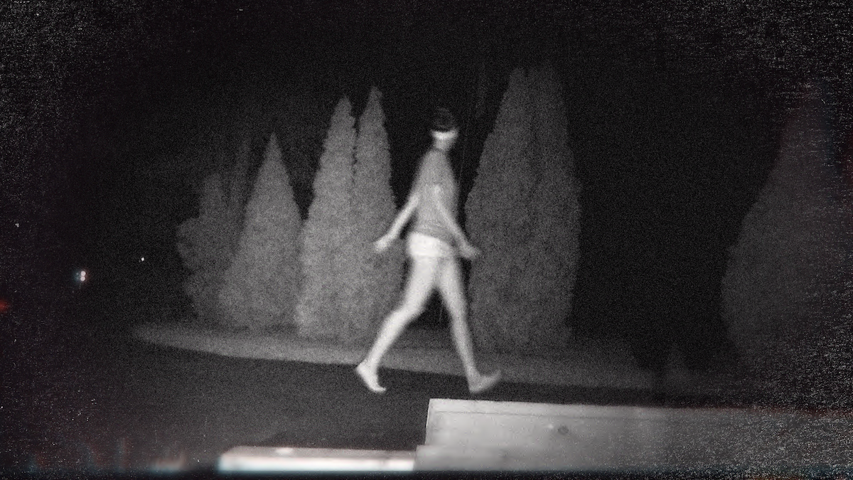 Production still from 'Unsolved Mysteries' Volume 3. Grainy black and white image of someone walking along a road.