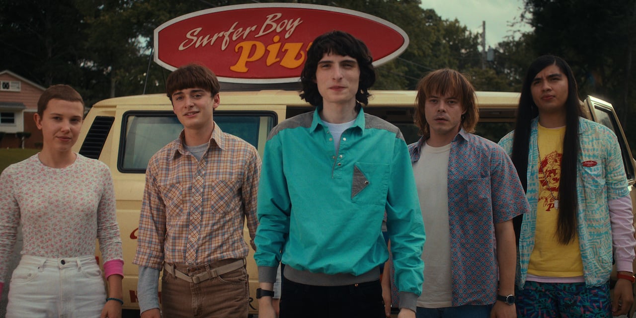 The cast of Stranger Things Season 4, one of the best Netflix shows of 2022, in front of the Surfer Boy Pizza van.