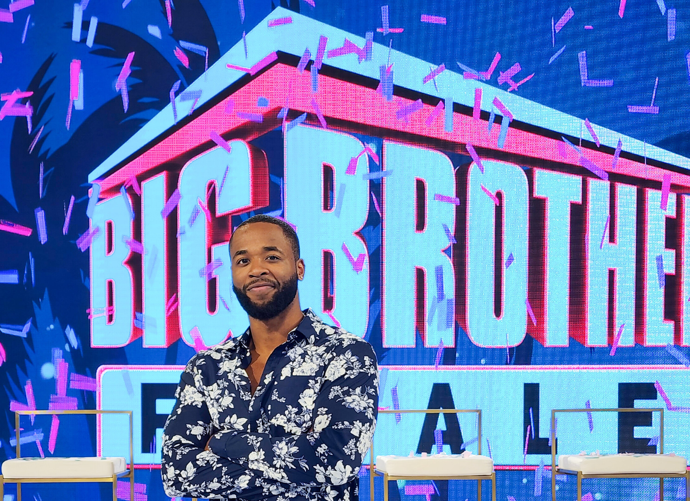 Monte Taylor poses in front of the 'Big Brother' finale screen with his arms crossed.
