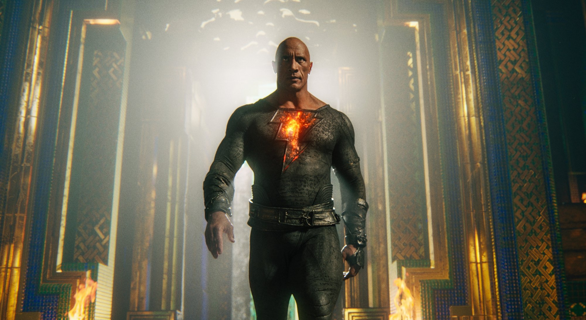 'Black Adam' Dwayne 'The Rock' Johnson as Black Adam with a glowing thunderbolt on his chest walking away from a bright light source.