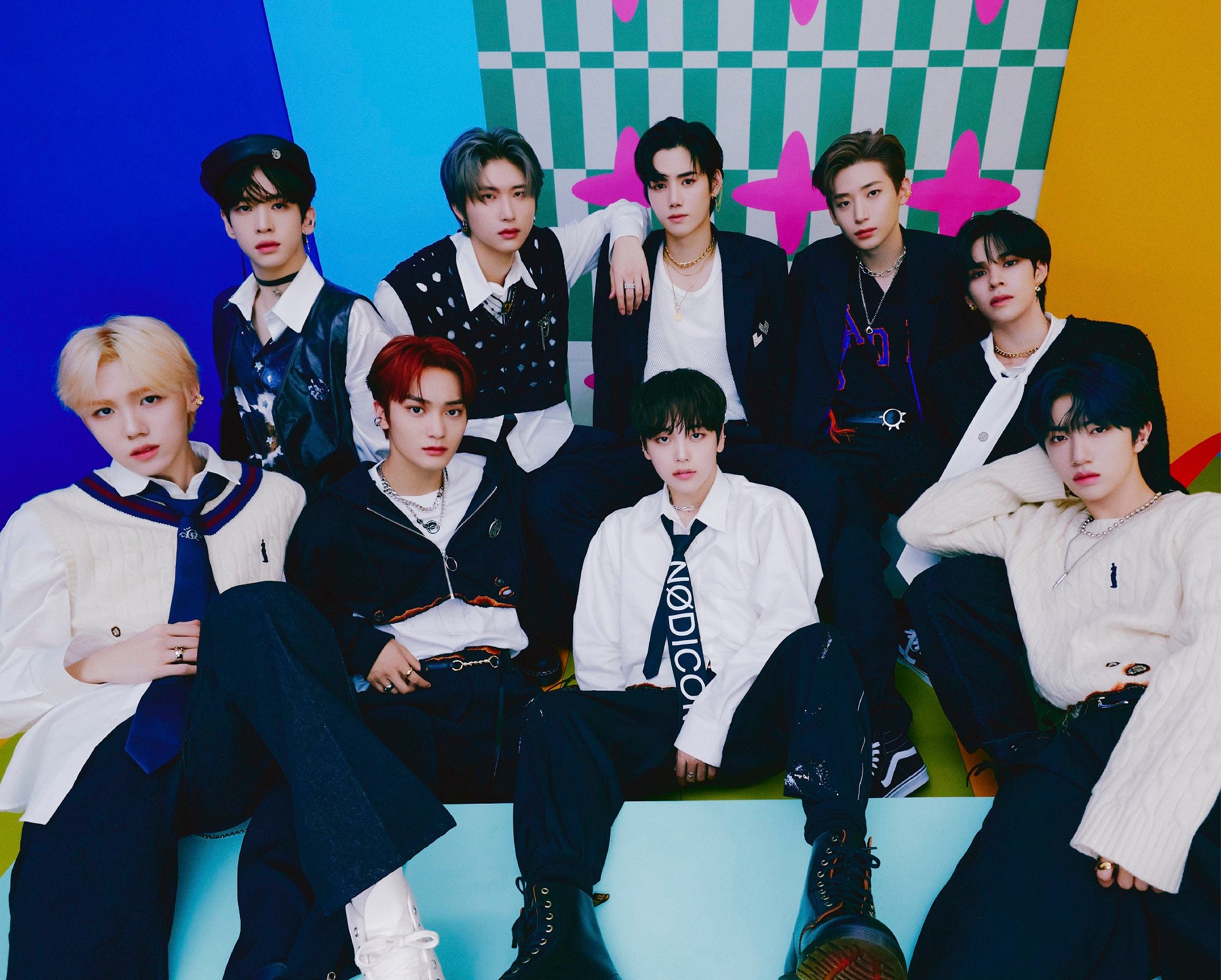 The members of CRAVITY pose in black-and-white outfits in front of a colorful background