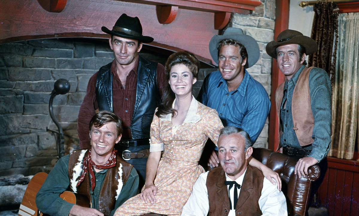 Group photo of 'The Virginian' cast members in front of a fireplace
