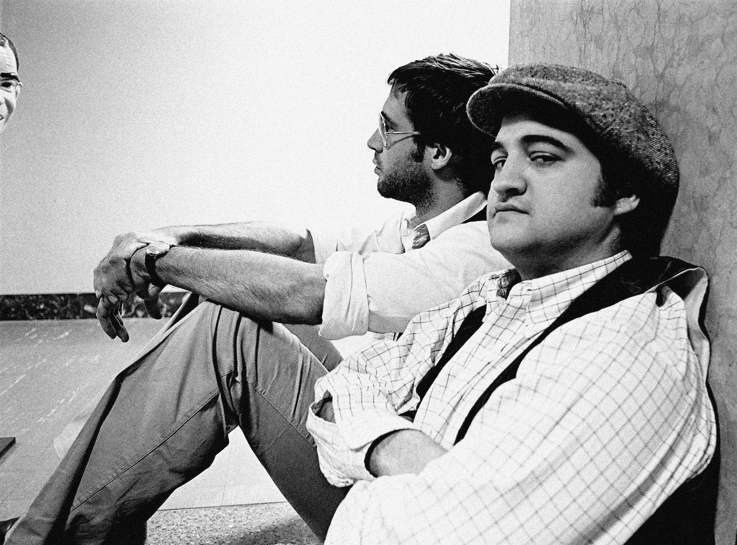 Chevy Chase and John Belushi sitting against a wall during a break from 'Saturday Night Live'