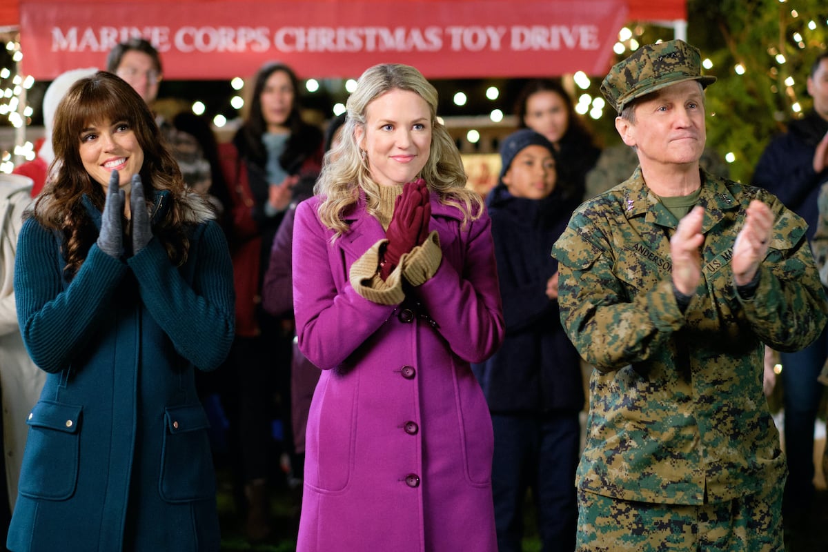 Erin Cahill in a purple coat standing next to a man in military uniform in Hallmark's 'Christmas Bedtime Stories'
