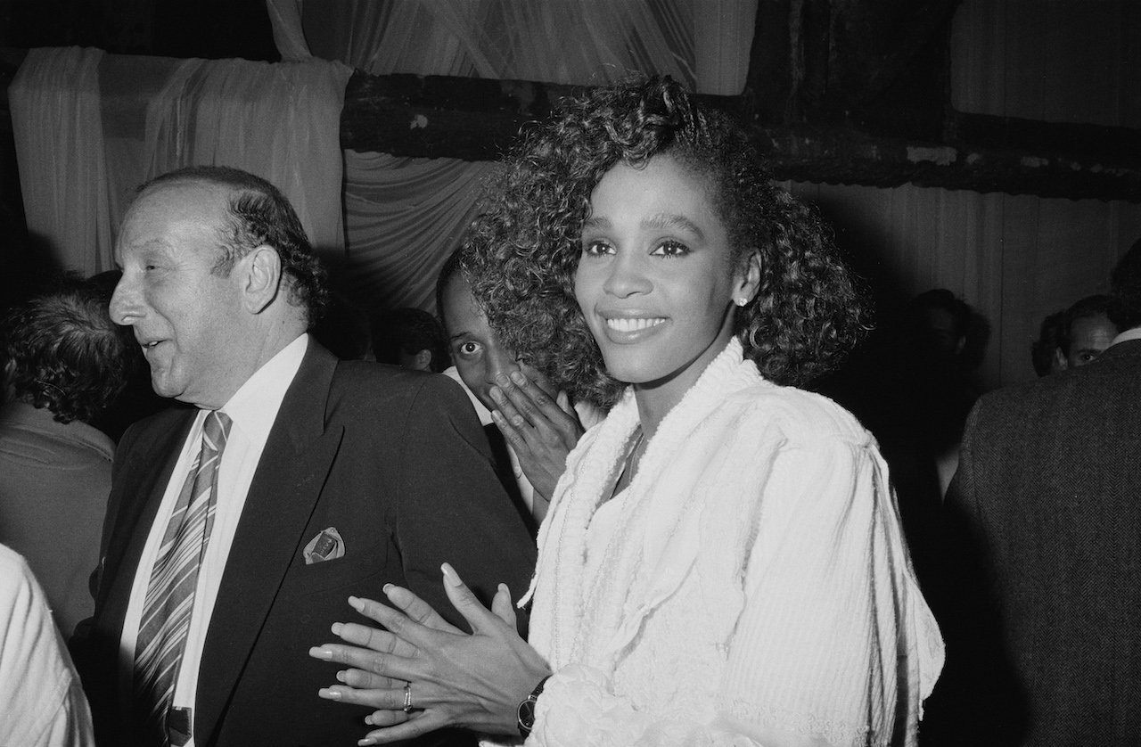Clive Davis and Whitney Houston smile and mingle with others at industry event; Davis remembers the first time he heard Houston sing