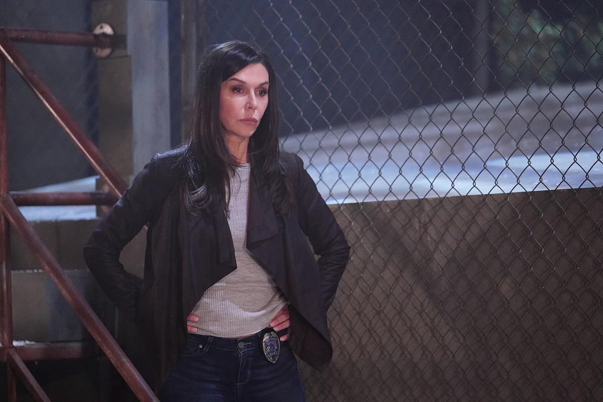 'General Hospital' star Finola Hughes in jeans, a grey shirt, and black jacket; stands in front of an alleyway staircase.