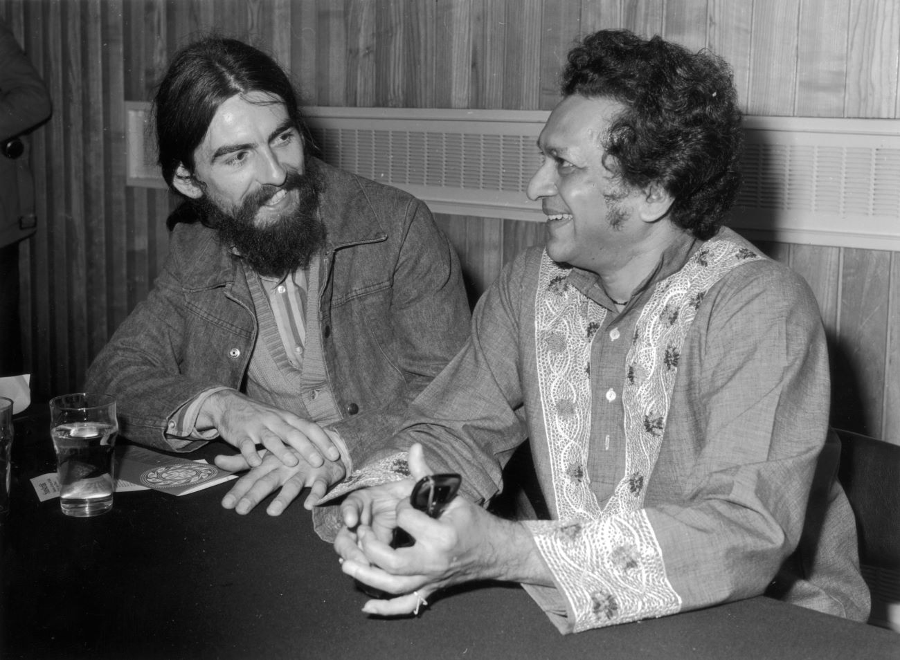 A black and white picture of George Harrison and Ravi Shankar sitting at a table together.
