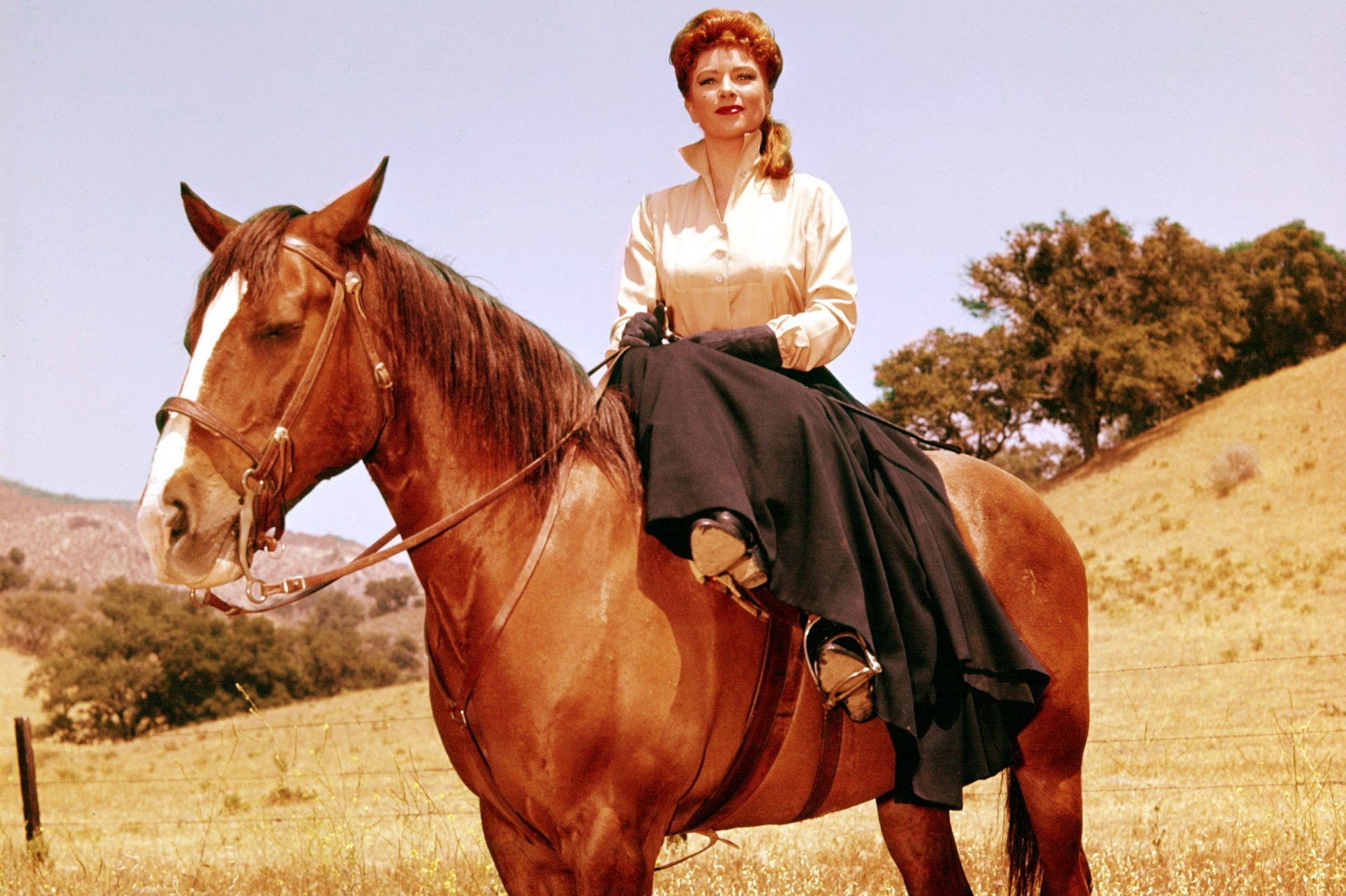 'Gunsmoke' Amanda Blake as Kitty Russell wearing a white top and black skirt side-saddled on a brown horse