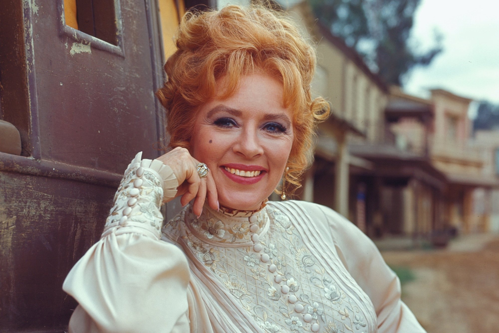'Gunsmoke' Amanda Blake as Kitty Russell with her arm resting on a carriage as she's smiling.