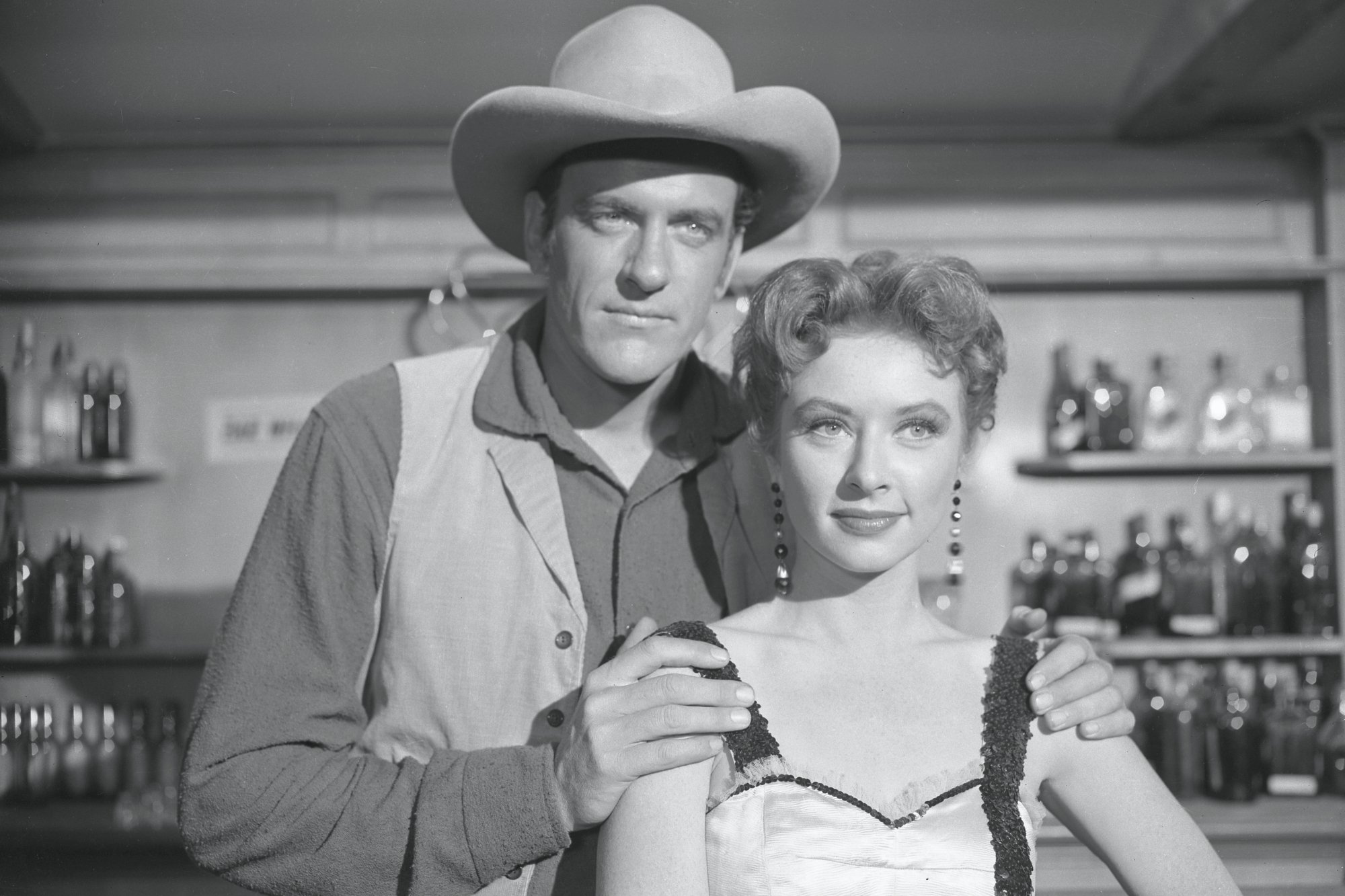 'Gunsmoke' James Arness as Marshal Matt Dillon and Amanda Blake as Kitty Russell. He's standing just behind her with his hands on her shoulders. They're both wearing Western costumes.