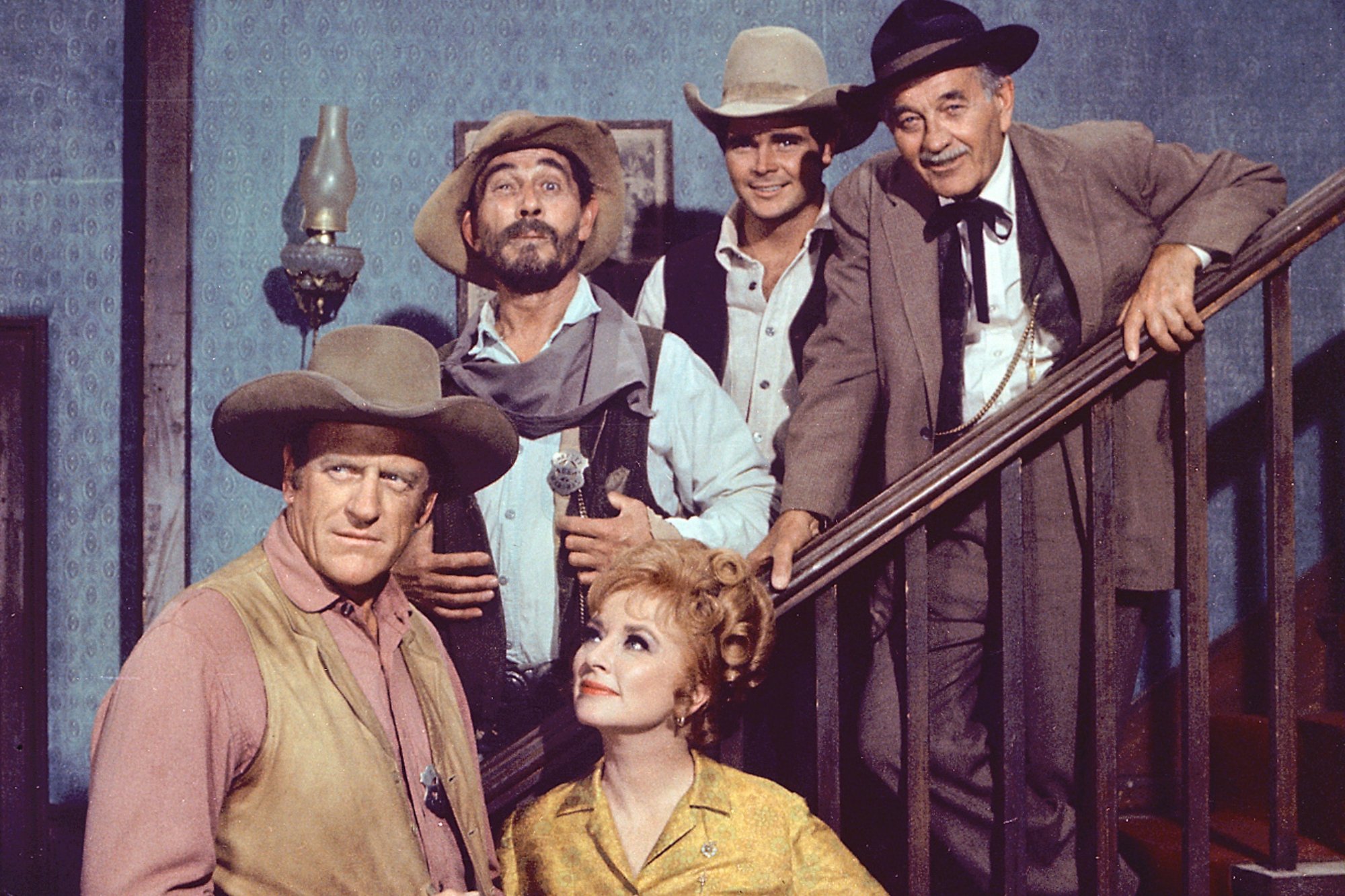 'Gunsmoke' James Arness as Matt Dillon, Amanda Blake as Kitty Russell, Ken Curtis as Festus Haggen, Buck Taylor as Newly O'Brien, and Milburn Stone as Dr. Galen Adams standing on a staircase, posing.