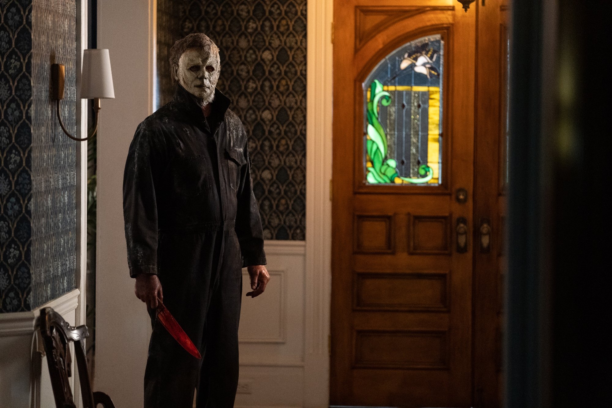 'Halloween Ends' James Jude Courtney as The Shape/Michael Myers standing in an entryway wearing his mask, holding a bloodied knife.