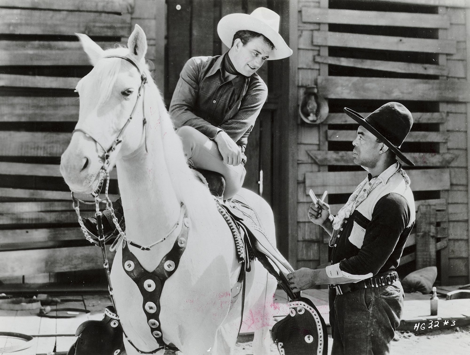 'Haunted Gold' John Wayne as John Mason in horror movie. Wayne is sitting on top of a white horse wearing a cowboy outfit, talking to another cowboy in uniform.