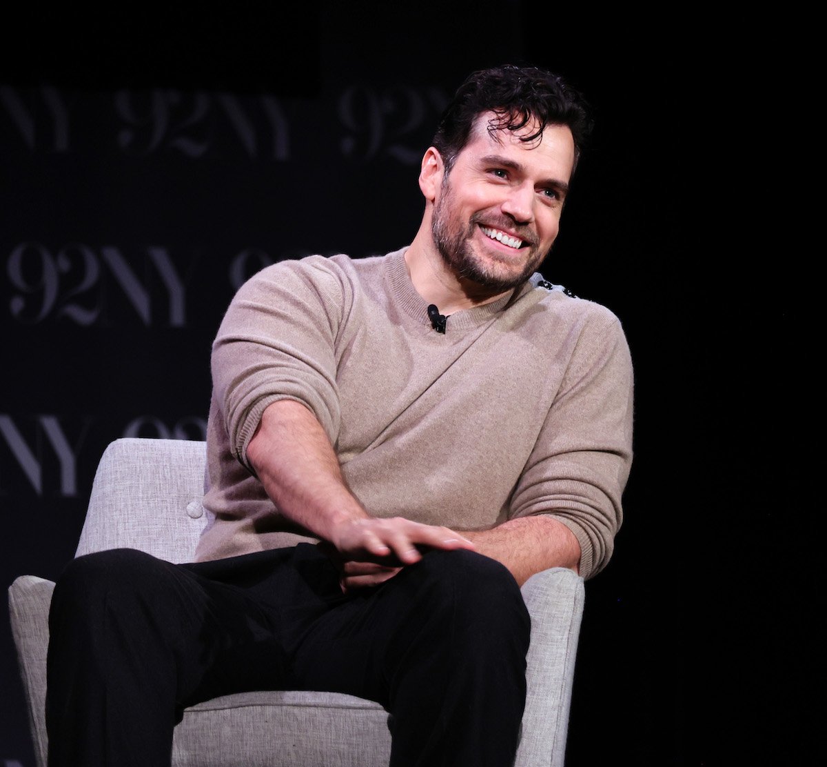 Henry Cavill sits in a chair and smiles about his Superman cameo on the 'Happy Sad Confused' podcast