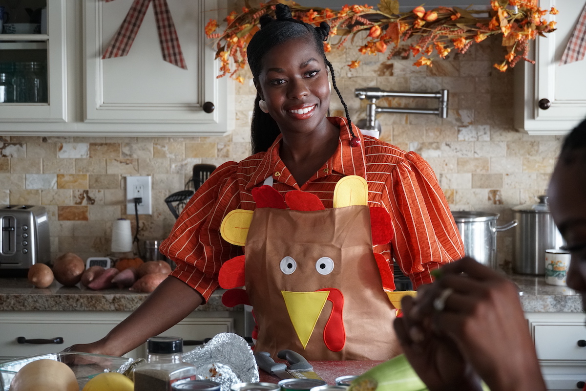 A smiling Black woman wearing a Thanksgiving apron in the BET+ movie 'Holiday Hideaway'