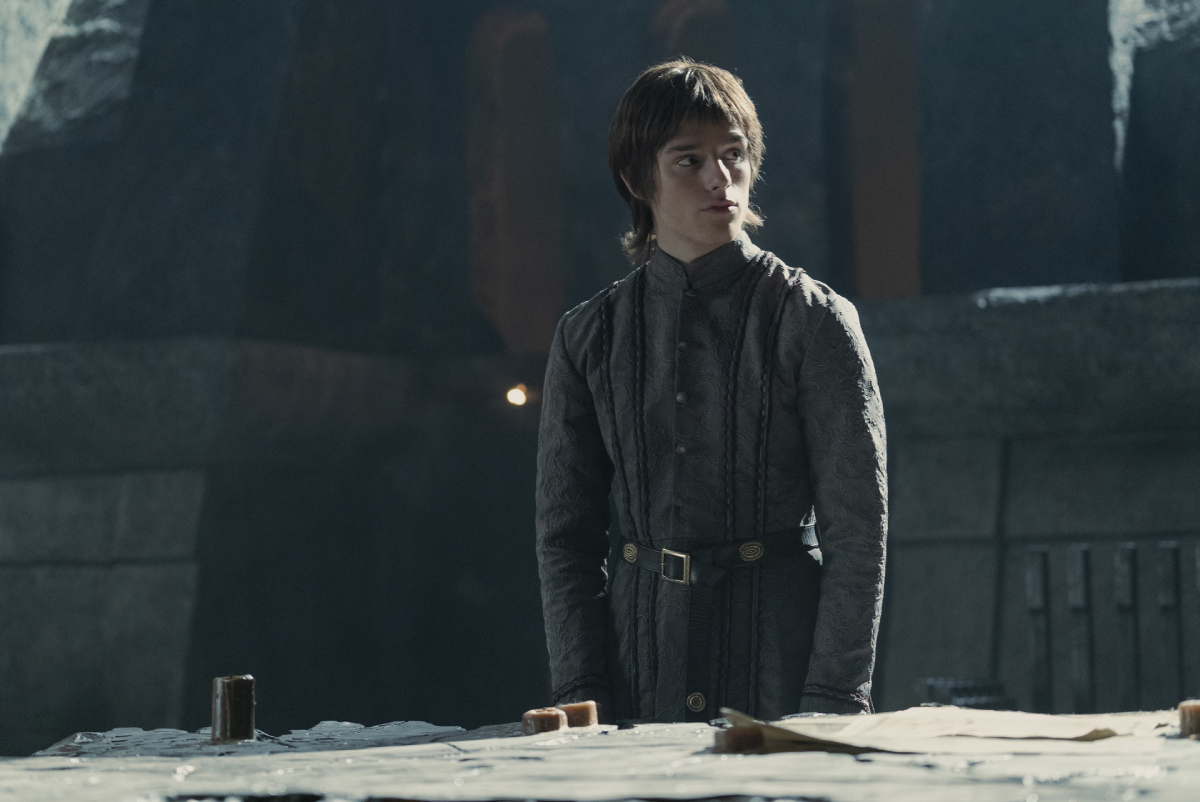 In House of the Dragon Episode 8 Harry Collett plays Jacaerys Targaryen. Jacaerys stands behind a table. 