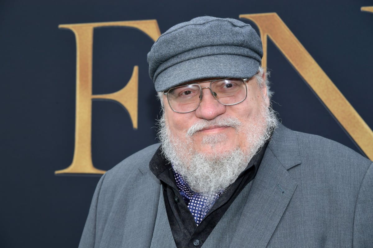 House of the Dragon is based on George R.R. Martin's book Fire & Blood. Martin wears a grey hat and suit jacket and glasses.