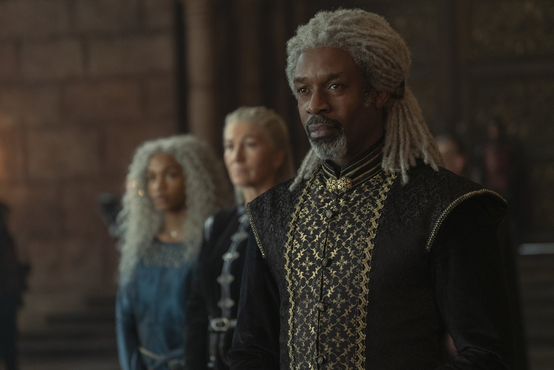 Wil Johnson as Vaemond Velaryon in 'House of the Dragon' Episode 8. He's standing in front of his brother's family and wearing a black vest embroidered with gold.