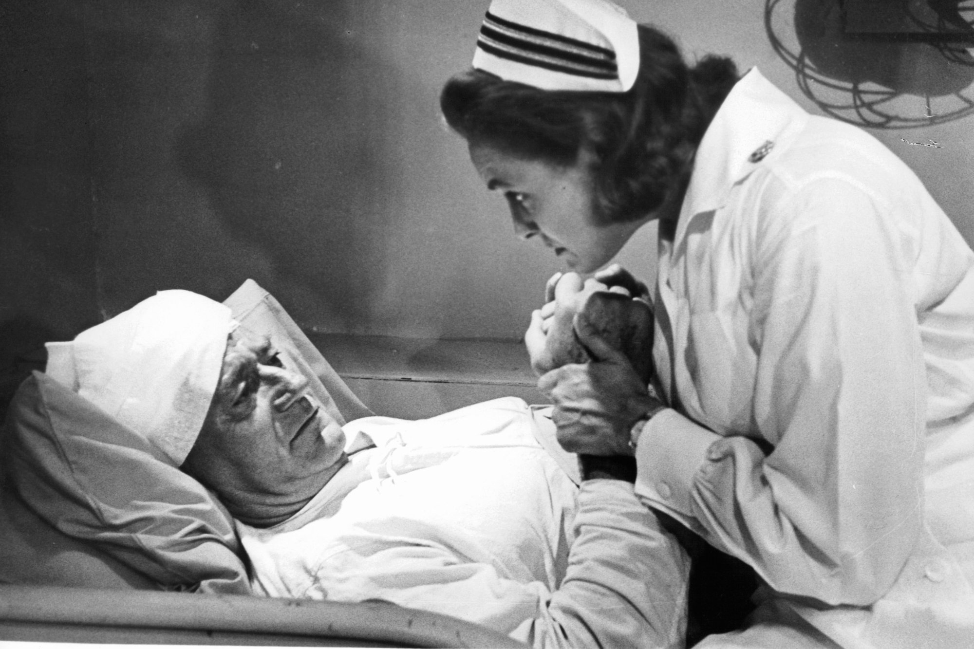 'In Harm's Way' John Wayne as Rock and Patricia Neal as Maggie. He's laying in bed with bandages on his head. She's wearing a nurse outfit, holding onto his hands.