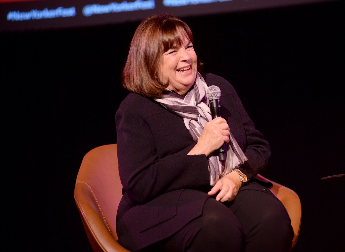 Ina Garten, who once said she didn't 'miss' running her Barefoot Contessa store because it was 'very intense', smiles and looks on while sitting in a chair and holding a microphone