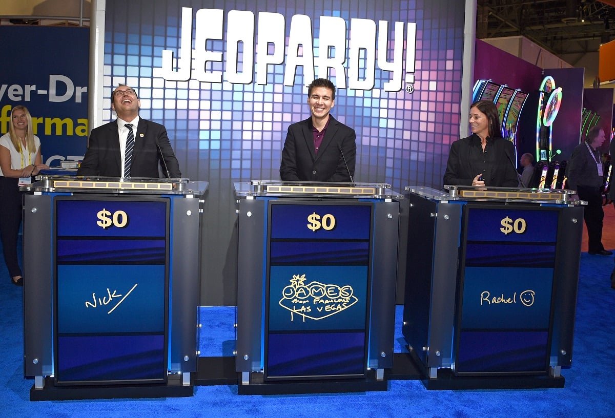 'Jeopardy' champion James Holzhauer dressed in a black suit competes with two other contestants at a fan expo.