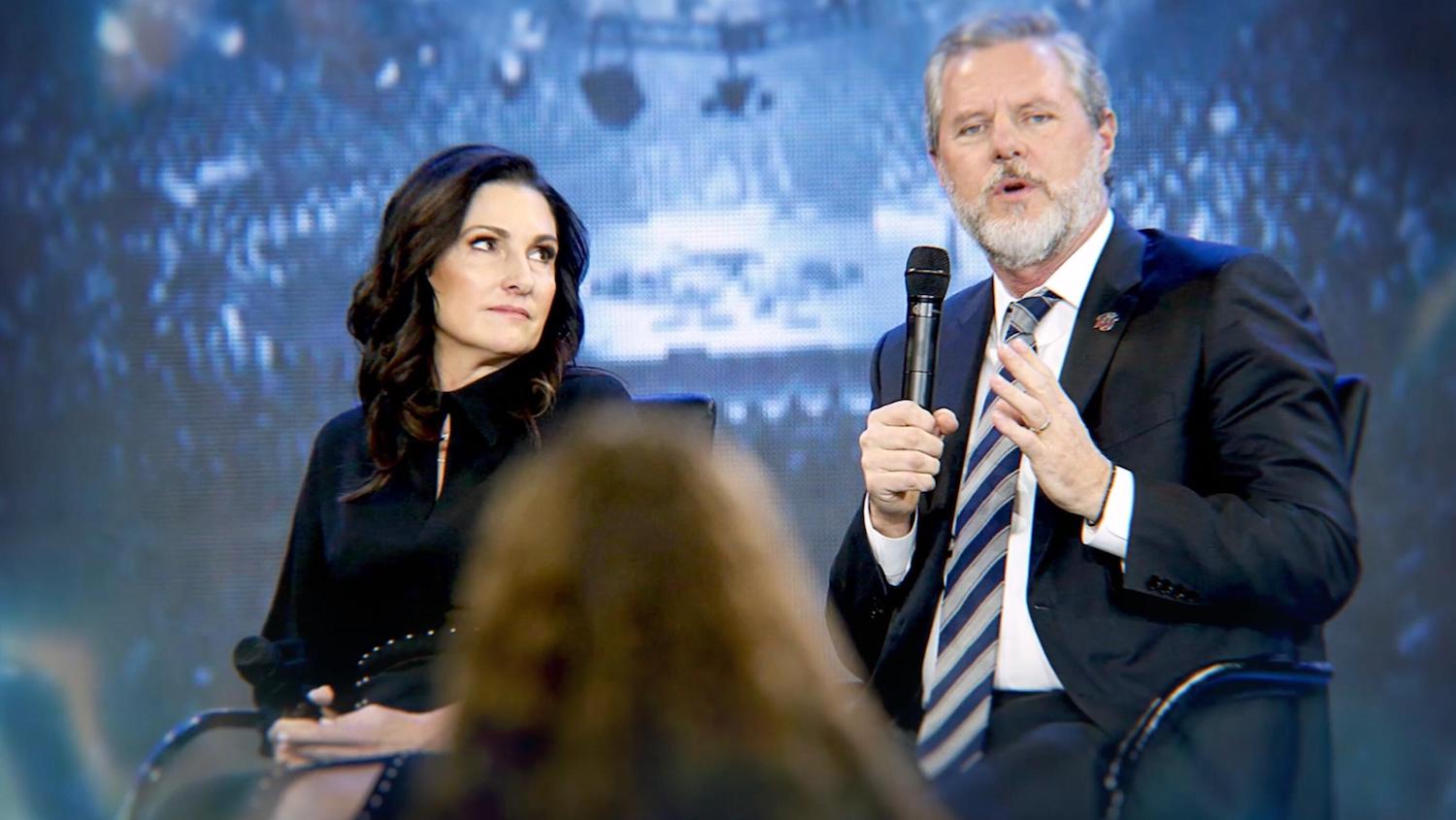'God Forbid: The Sex Scandal That Brought Down A Dynasty' production still shows Becki Falwell sitting next to Jerry Falwell Jr. while he holds a microphone on stage.