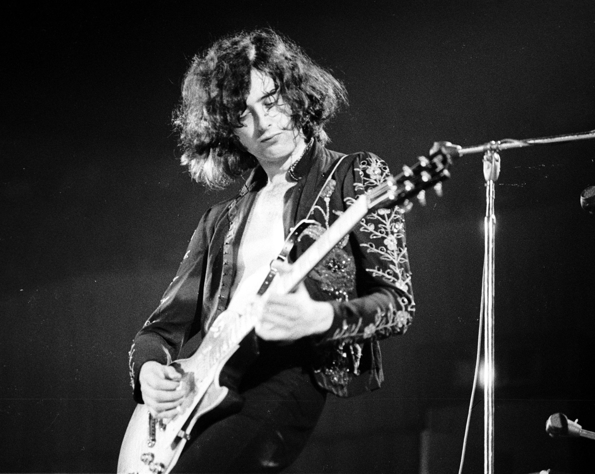 A black-and-white photo of Jimmy Page playing guitar on stage