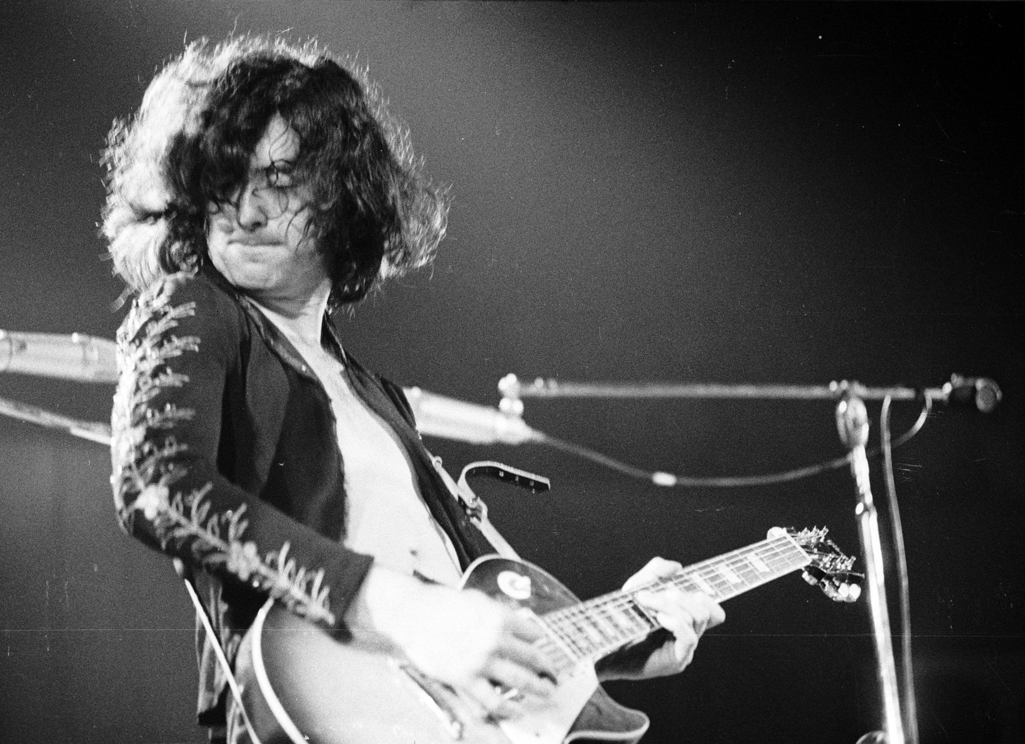 A black-and-white photo of Jimmy Page playing guitar on stage