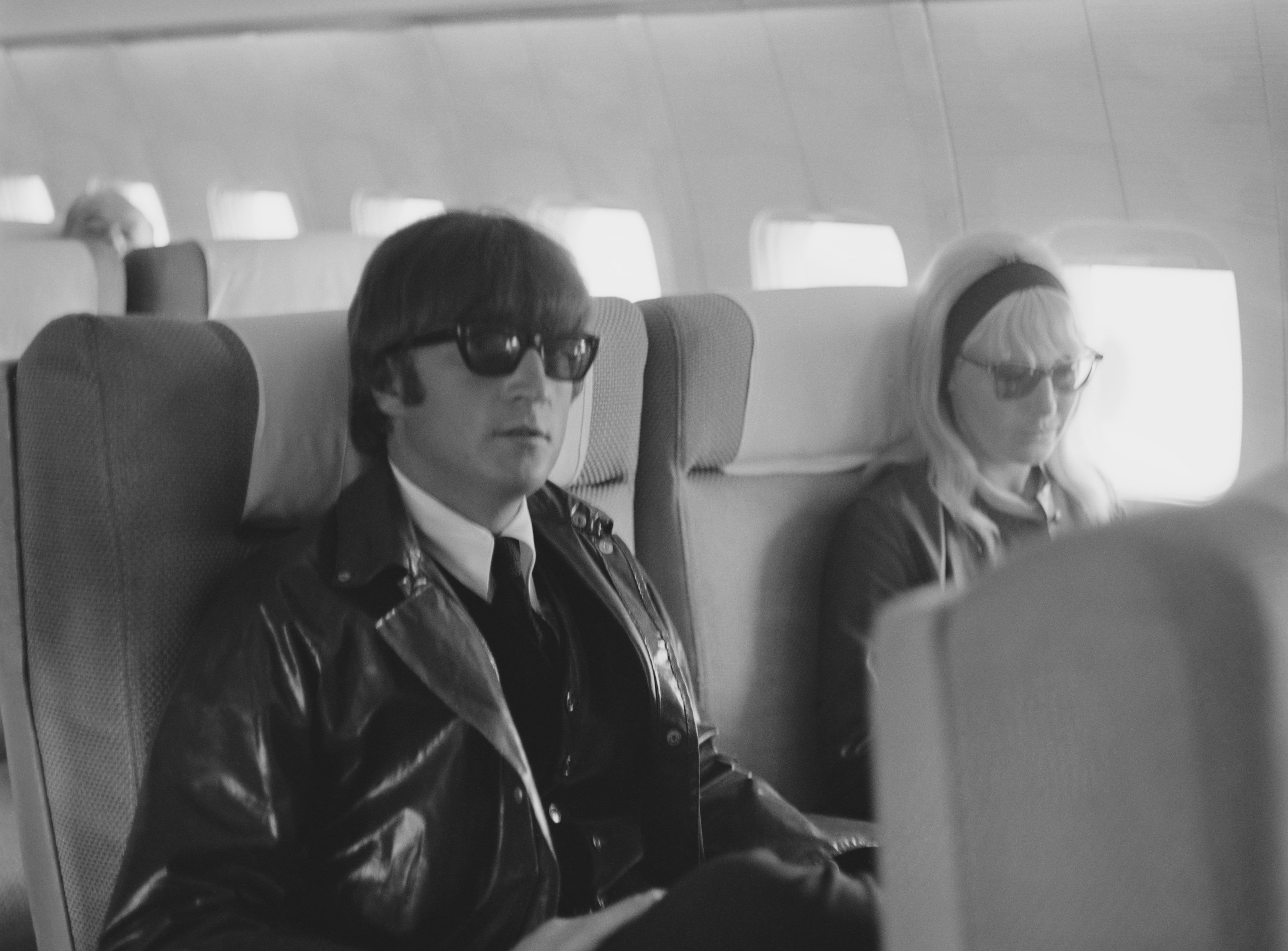 English singer, songwriter, and peace activist John Lennon (1940 - 1980) of the Beatles with his wife Cynthia (1939 - 2015) sitting on an airplane