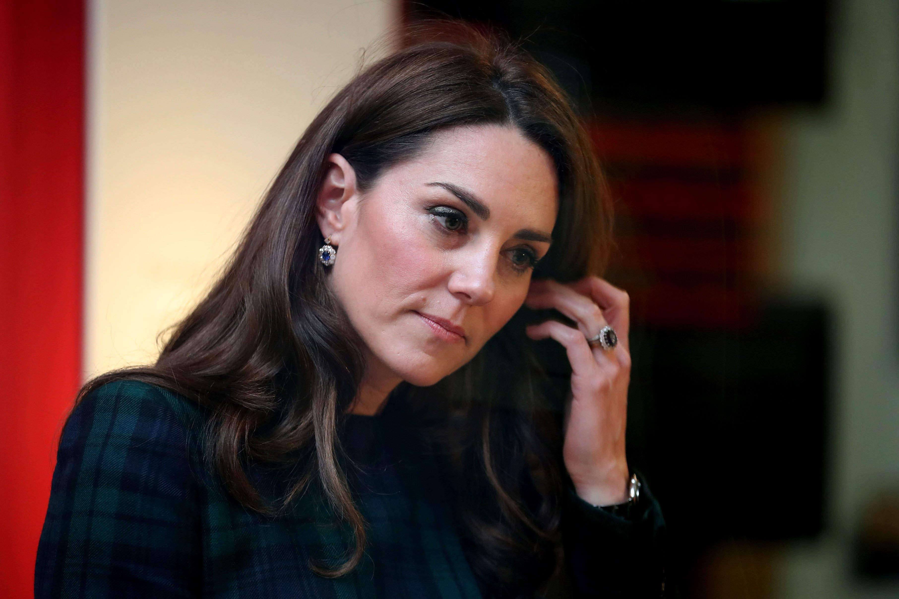 Kate Middleton touches her hair and looks away.