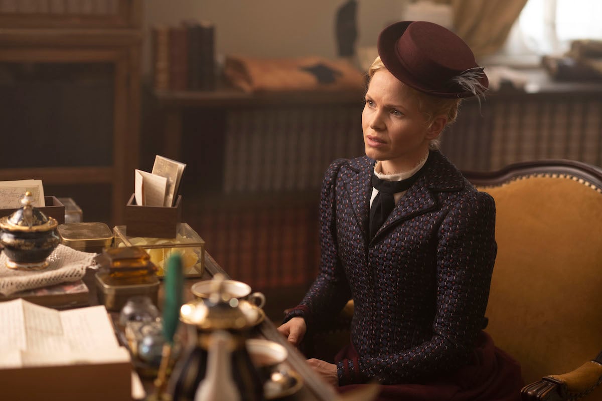 Kate Phillips as Eliza Scarlet, wearing a hat and sitting at a desk, in 'Miss Scarlet and The Duke' Season 2