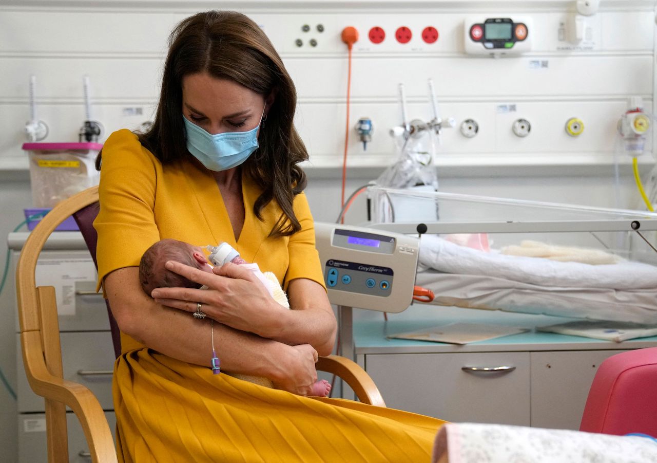 Kate Middleton, Princess of Wales, wearing a face mask to help mitigate the possible spread of Covid-19, speaks to a new mother, whilst holding newborn Bianca, during a visit to the Royal Surrey County Hospital's maternity unit