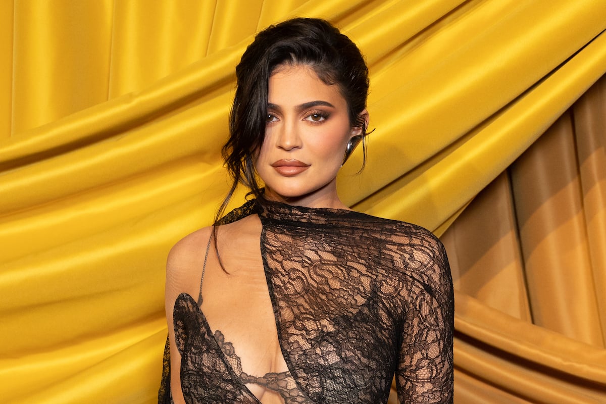 Kylie Jenner, whose son's name is still unknown, poses in a black dress in front of a gold background.