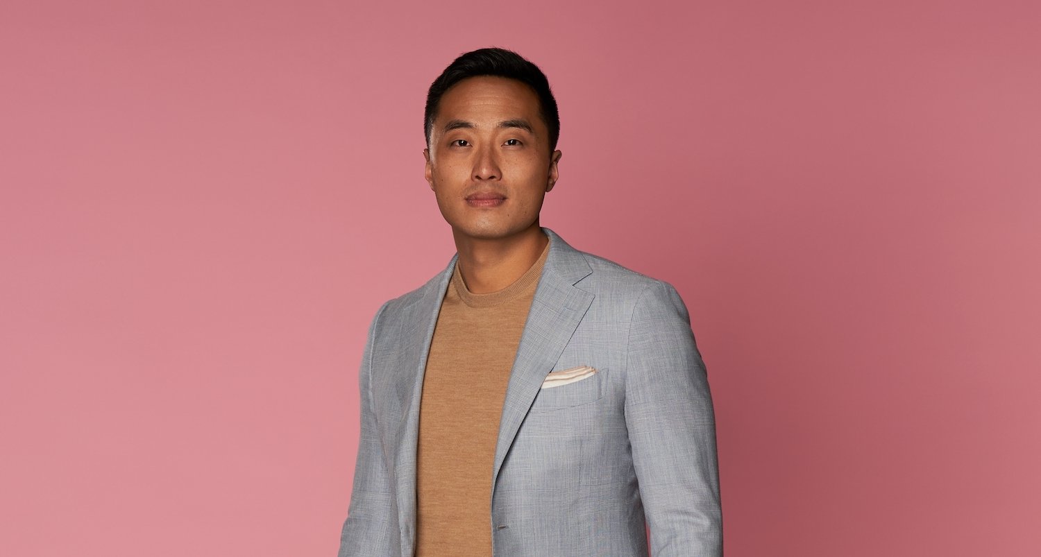 'Love Is Blind' Season 3 star Andrew wearing a gray blazer, tan shirt, and standing in front of a pink background.