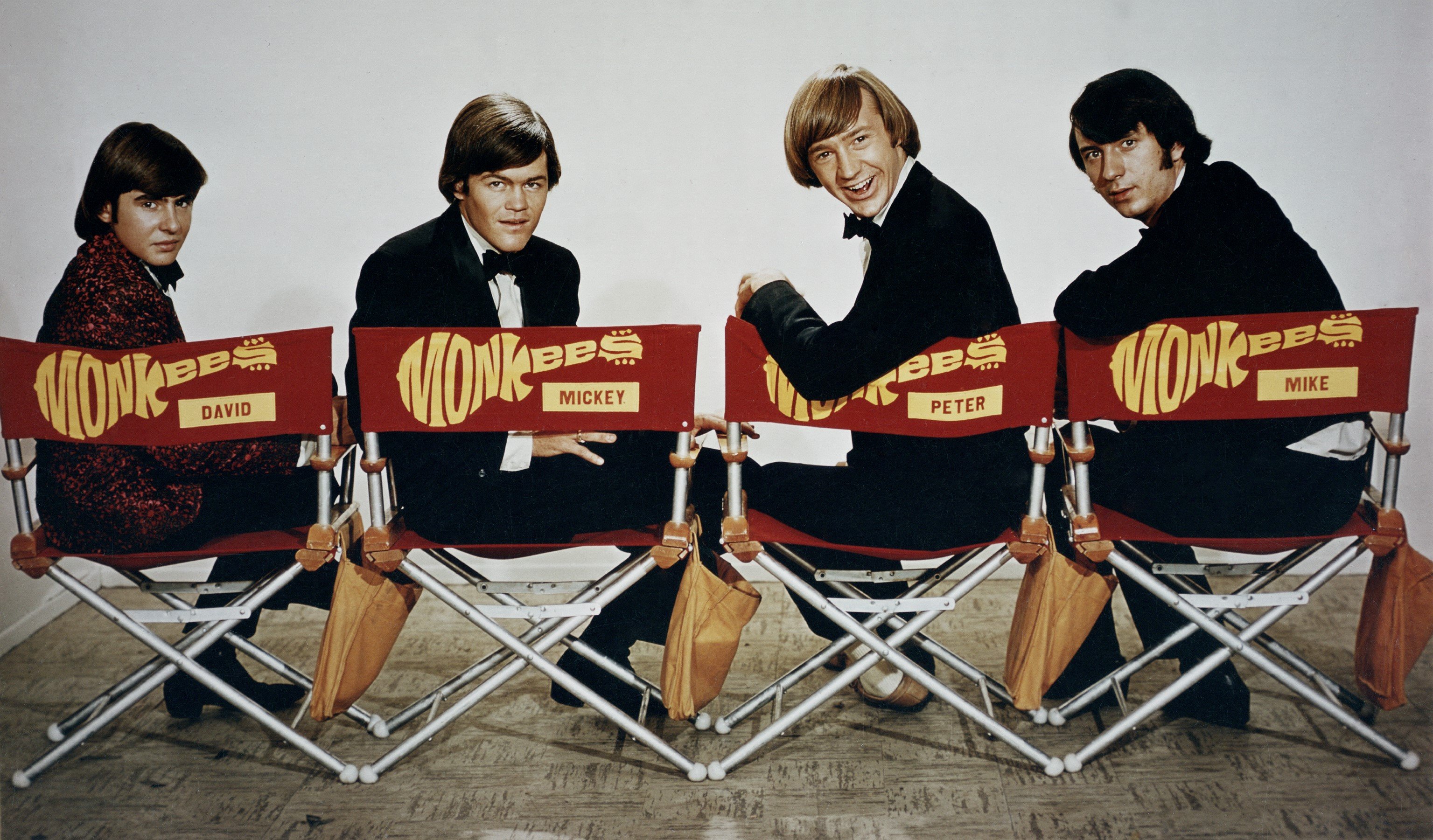 The Monkees' Davy Jones, Micky Dolenz, Peter Tork, and Mike Nesmith sitting in chairs